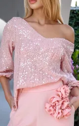 Blusa color rosa pálido con lentejuelas, escote asimétrico dejando un hombro al descubierto y mangas 3/4 con puños elásticos.