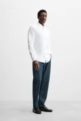Camisa blanca de algodón, corte regular, con cuello italiano abierto, manga larga con puños abotonados y cierre frontal con botones.