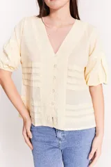 Blusa de color amarillo, con diseño de tablas en el torso y mangas abullonadas.