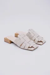 Mules color crudo con capellada trenzada de cuero y taco de madera de 3 cm.