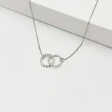 Gargantilla de plata con cadena de eslabones y dos dijes circulares entrelazados, uno liso y otro con textura trenzada.
