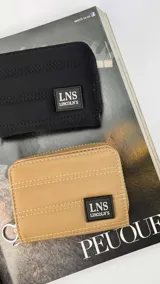 Billetera corta con cierre alrededor y tapa, confeccionada en tela capitoneada. Incluye varias reparticiones con tarjeteros y bolsillos internos, y una correa de mano desmontable. Disponible en negro, rojo y dorado.