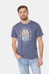 Remera blanca de manga corta con cuello redondo y un estampado gráfico frontal que simula un paisaje costero con un sol naciente o poniente, rodeado por texto circular que dice "SURF - LIFE UNDER THE SUN - CLUB".