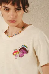 Remera color crema de manga corta con cuello redondo y estampado de hongos bordados en el frente.