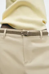 Pantalón chino color amarillo claro, de tiro medio, con bolsillos frontales y traseros. Incluye cinturón trenzado marrón.