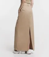 Pollera larga color beige, de tiro alto, corte recto y confeccionada en sarga ligera. Presenta trabillas en la cintura, cierre con botón y cremallera, y abertura en la parte posterior.