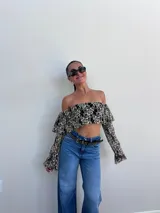 Top corto negro con diseño de encaje floral en blanco, escote bardot y mangas largas acampanadas.