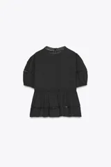 Blusa negra de algodón con cuello redondo y manga corta abullonada. Presenta bordados a tono y cierre en la espalda con abertura y botón.