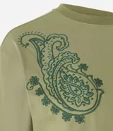 Remera boxy de algodón color verde oliva, con cuello redondo y mangas cortas. Presenta un bordado paisley en el hombro izquierdo.