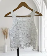 Musculosa corta blanca de tejido de punto calado, con diseño de flores y flecos en el ruedo.