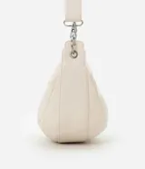 Bolso mediano color crema, con forma de media luna y correa ajustable con aros metálicos.
