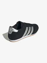 Zapatillas Adidas Taekwondo Lace negras de gamuza con las tres rayas plateadas y refuerzo plateado en el talón.