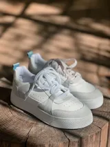 Zapatillas urbanas blancas con detalles en gris, suela plana y cordones blancos.