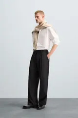 Pantalón negro de corte amplio con cinturón de tela con hebilla metálica. Presenta pliegues frontales, bolsillos laterales y traseros. Cierre frontal con cremallera y botón.