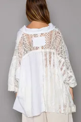 Camisa blanca de manga larga con detalles de encaje y crochet, cuello con escote en V y cierre frontal con botones. Diseño oversized con dobladillo asimétrico.