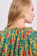 Blusa de manga larga con estampado floral en tonos mostaza, verde y rosa. Tiene cuello redondo con lazo ajustable.