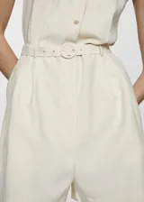 Mono corto color crema, sin mangas, con cuello camisero, cierre frontal con botones y cinturón ajustable.