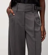 Pantalón de vestir gris oscuro, modelo wide leg, con cintura traspasada y hebilla metálica. Presenta pliegues delanteros marcados y bolsillos traseros.