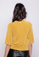 Top color mostaza de manga 3/4 y cuello polera, confeccionado en tela con pequeños destellos metálicos.