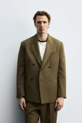 Blazer color verde oliva de corte regular, confeccionada en tejido con lana. Presenta cuello con solapas de pico, manga larga con puños abotonados, bolsillo de vivo en pecho, bolsillos de doble vivo en cadera, bolsillo interior y aberturas en la espalda. Cierre frontal cruzado con doble botonadura.