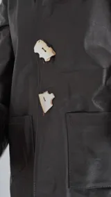 Blazer de cuero color gris oscuro, con aberturas laterales, aplique tipo pin desplegable bañado en bronce y botones de nácar.