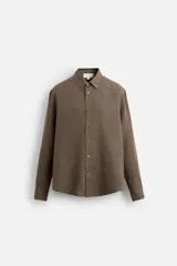Camisa color arena de lino con cuello abotonado, manga larga con puños abotonados, corte regular y bajo con aberturas laterales.