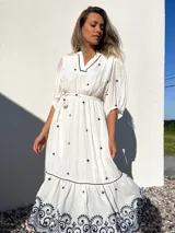 Vestido largo blanco con bordados azules, escote en V, mangas 3/4 abullonadas y lazo en la cintura.