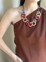 Collar con aros de acrílico entrelazados con tiento sintético color chocolate. Tiene nudo ajustable para regular el largo.