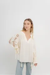 Blusa color crema con escote en V, mangas largas con detalles calados y puños elásticos.