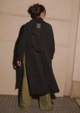Trench negro confeccionado en algodón y nylon, repelente al agua, con largo midi, tajos laterales y bolsillos internos altos.
