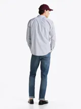 Camisa de mangas largas a rayas verticales azules y blancas, confeccionada en popelín de puro algodón con tecnología Flex que le confiere elasticidad. Tiene cuello abotonado, puños redondeados con botón y logo de Tommy Hilfiger bordado en el pecho.