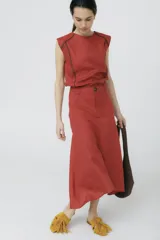 Falda midi color ladrillo, de corte evasé y tiro alto, con bolsillos laterales y botón decorativo en la cintura.