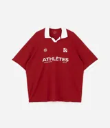 Remera de manga corta estilo polo, color rojo, con cuello y puños en contraste blanco. Presenta un corte oversized con hombros caídos y la palabra "ATHLÈTES" estampada en blanco en el frente. Incluye pequeños gráficos blancos a cada lado del pecho.