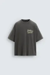 Camiseta gris oscuro con efecto lavado, cuello redondo y manga corta. Tiene un bolsillo en el pecho y estampados en el frente y la espalda.