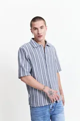 Camisa de manga corta con corte oversize, a rayas verticales blancas y grises, con cuello clásico y cierre frontal con botones. Confeccionada en algodón.