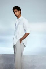 Camisa blanca de popelina de algodón con cuello inglés, tapeta clásica, dos bolsillos superiores abiertos, canesú con pliegue de caja en la espalda, mangas largas con puños abotonados, tapeta de manga con botón y bajo levemente redondeado. Corte holgado.