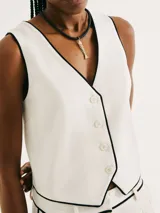 Chaleco blanco con ribete negro, cuello en V y cierre frontal con botones.