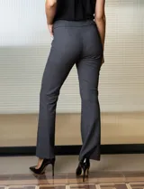 Pantalón largo de vestir negro con finas rayas verticales blancas, corte flared de tiro alto y aplique de cadena dorada en la cintura.