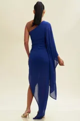 Vestido largo de fiesta fucsia, con un solo hombro y manga larga tipo capa. Tiene un corte ajustado con drapeado en la cintura y abertura lateral en la falda.