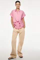 Camisa fluída color rosado confeccionada en hilatura con modal. Tiene cuello solapa, manga corta con vuelta y detalle de nudo en el delantero. Cierre frontal con botones.