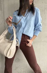 Camisa celeste de manga larga con cuello mao y cierre frontal con botones. Presenta detalles de broderie en el frente y mangas.