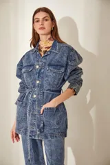 Campera de denim celeste con efecto nevado, corte recto, cuello clásico, cierre frontal con botones metálicos, cuatro bolsillos frontales con solapa y cinturón de la misma tela con hebilla metálica.