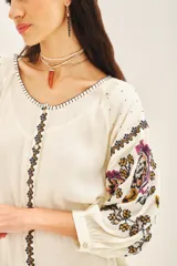 Vestido corto de bambula color celeste claro con bordados florales multicolor en el frente y mangas. Presenta escote redondo con cartera, cinturón de tela ajustable y volado en el ruedo.