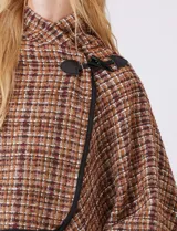 Ruana tejida de la marca Jones New York, con estampado a cuadros en tonos marrón, beige y blanco. Presenta cuello alto y cierre frontal con botón trenca y botón a presión interno. Los bordes están ribeteados en negro.