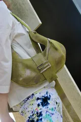 Cartera bandolera de cuero color verde oliva con efecto desgastado. Tiene forma de media luna, asa larga regulable, cierre superior con cremallera y broche imán metálico.