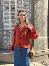 Blusa color terracota de muselina con escote en V y lazos para ajustar. Tiene mangas largas abullonadas con volados en los puños.