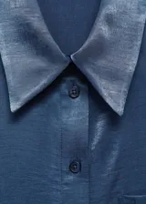 Camisa azul sin mangas de tejido fluido y satinado, con cuello camisero, cierre frontal con botones y bolsillo de parche en el pecho.