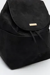 Mochila negra de símil gamuza con textura tipo reptil, diseño minimalista con solapa, cordón ajustable y bolsillos laterales.