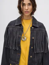 Campera de jean negra con cuello camisero, cierre frontal con botones metálicos y flecos en la parte delantera.