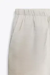 Pantalón palazzo color verde oliva de tejido fluido, tiro medio, cintura elástica ajustable con cordones y bolsillos laterales.